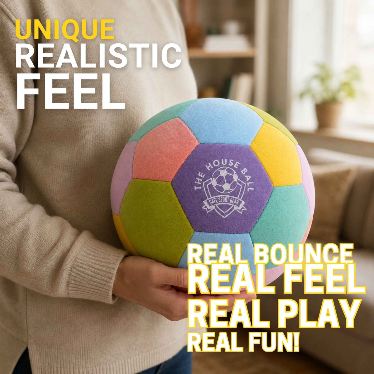 A person in a beige sweater holds a colorful plush soccer ball with pastel panels and a purple center logo reading 'The House Ball'. The background is a softly blurred living room, with promotional text overlays reading 'Unique Realistic Feel' and 'Real Bounce Real Feel Real Play Real Fun!'.