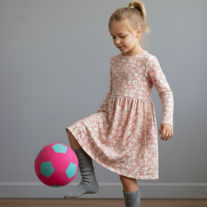 Young girl in a floral dress playing with The Pink House Ball against a plain background